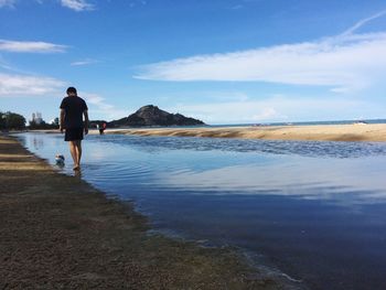 Rear view of man walking at beach against sky