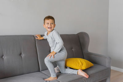 A five-year-old boy is having fun on the couch in the house and laughing loudly