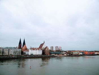 Buildings at waterfront against cloudy sky