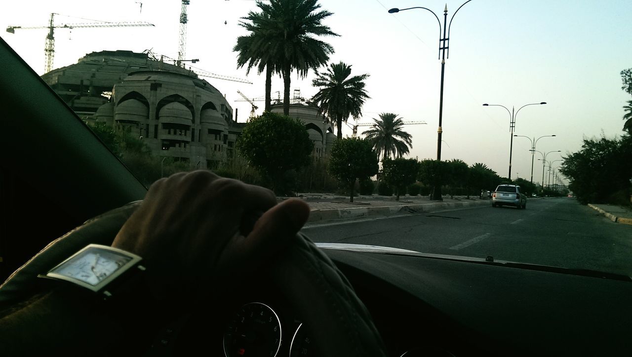 transportation, car, mode of transport, land vehicle, street, road, tree, building exterior, clear sky, architecture, travel, windshield, palm tree, built structure, sky, vehicle interior, part of, city