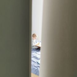 Boy studying while sitting bed seen through door gap
