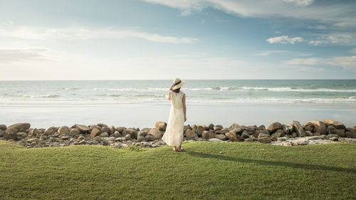 Rear view of woman standing by sea against sky