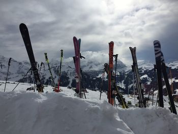 Ski poles on snowcapped mountain against cloudy sky