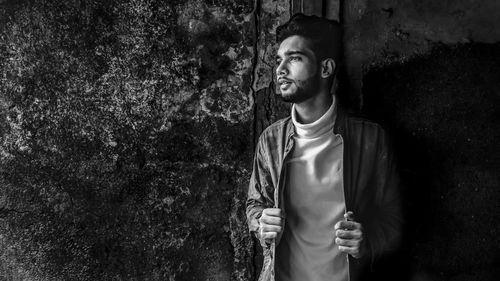 Portrait of young man looking away against wall