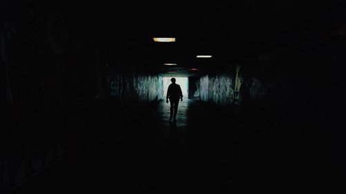 Rear view of silhouette man walking in illuminated tunnel