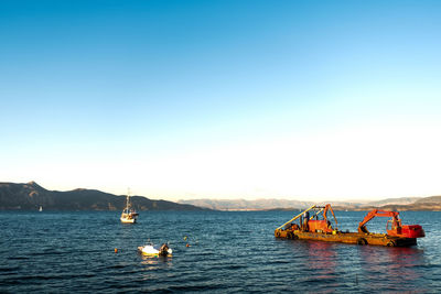 Boats in sea against clear blue sky