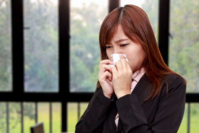 Young businesswoman sneezing against windows