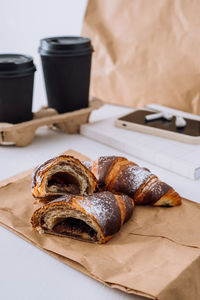 Chocolate croissants with cups of coffee and notepad with smartphone and earphones