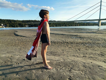 Full length of superhero boy standing on the beach at sunset. 