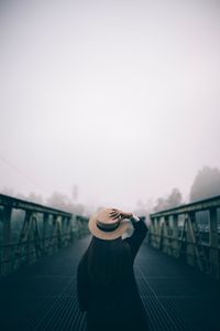 Woman standing on footbridge against sky