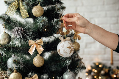 Cropped image of woman holding christmas ornament by tree