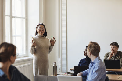 Smiling female teacher gesturing while teaching students in classroom