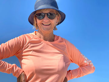 Low angle view of woman wearing sunglasses and sun hat against clear blue sky