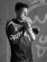 Young man looking away while standing against wall