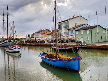 Boats moored at harbor by buildings against sky