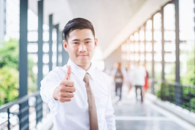 Portrait of young man showing thumbs up on footbridge