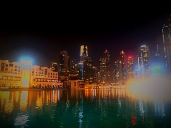 Illuminated buildings by river against sky at night