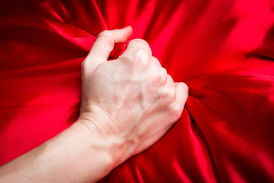 Cropped hand of woman holding red sheet on bed