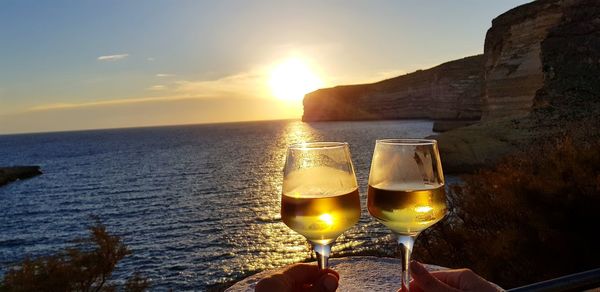 Cropped hands of couple holding alcohol at beach during sunset