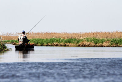 Rear view of man boat fishing in lake during sunny day