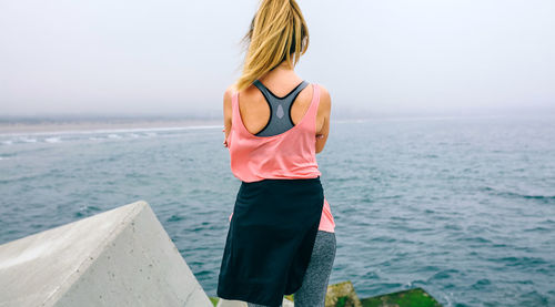 Rear view of woman standing by sea against sky