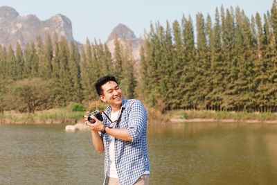 Portrait of smiling man holding lake against trees