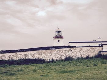 Lighthouse by building against sky