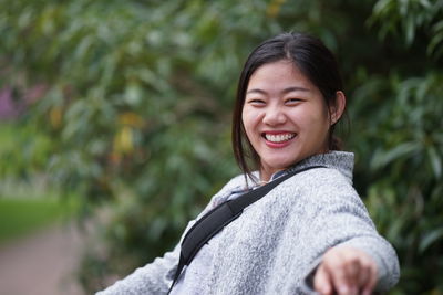 Portrait of cheerful young woman sitting on bench at park