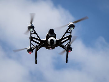 Low angle view of drone with camera flying against sky