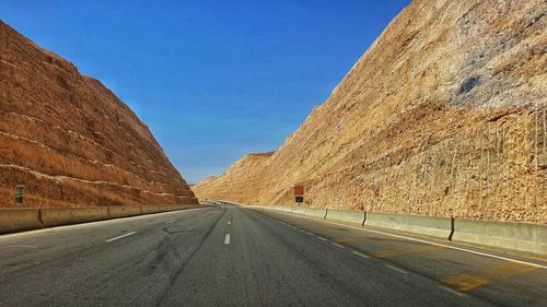 Empty road by mountain against clear sky