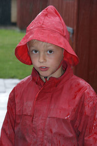 Portrait of boy wearing red raincoat standing outdoors during monsoon