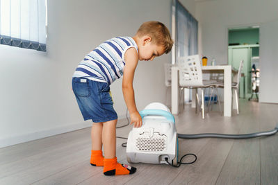 Full length of boy standing by vacuum cleaner at home