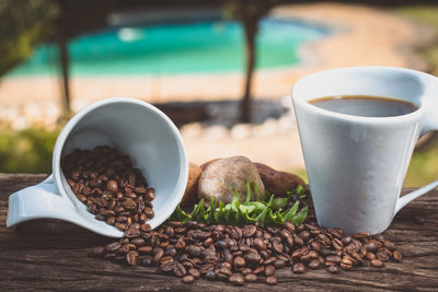 Beans spinning by black coffee on wood against trees