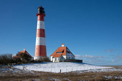 Lighthouse by sea against clear blue sky