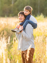 Father carries his son on shoulders. family time outdoors. man with child on field. dad and son