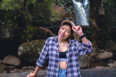 Portrait of young woman standing against waterfall