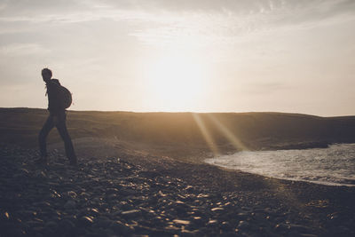 Man walking at beach against sky during sunset