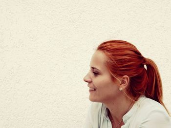 Close-up of smiling redhead woman by white wall