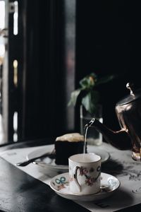 Close-up of teapot pouring tea in cup on table