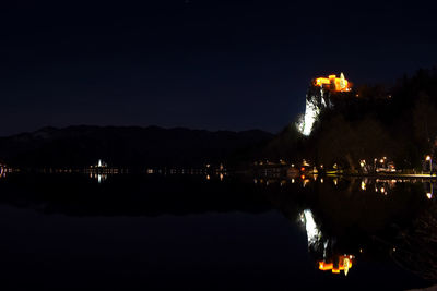 Illuminated buildings by lake against sky at night