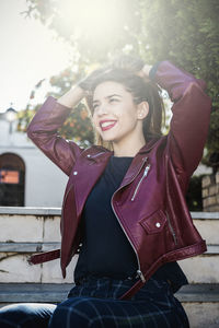 Smiling young woman with hands in hair wearing maroon jacket