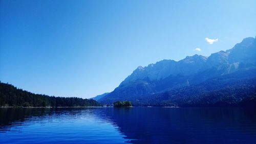 Scenic view of lake and mountains against clear blue sky