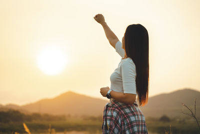 Side view of woman standing against sky during sunset