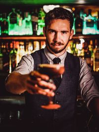 Portrait of bartender holding drink while standing in bar