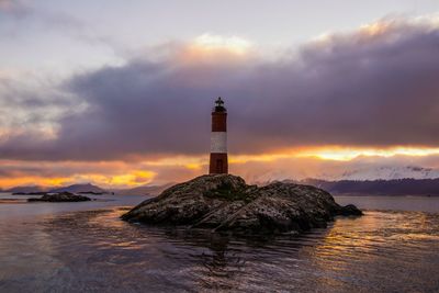 Lighthouse by sea against sky during sunset