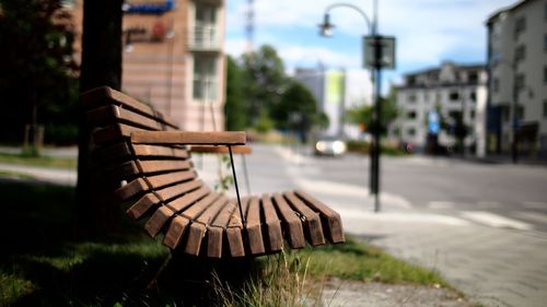 Empty wooden bench by street in city