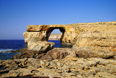 Stone wall by sea against clear blue sky