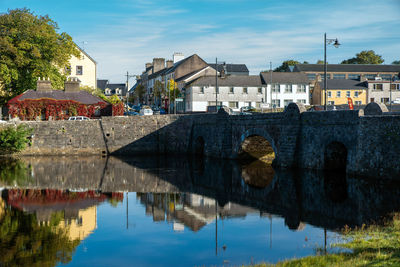 Arch bridge over river by buildings against sky in city