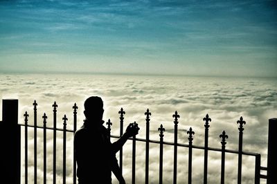 Silhouette of man on fence against sky
