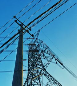 Low angle view of electricity pylon against clear blue sky